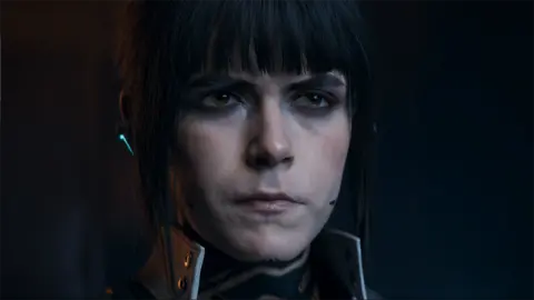 Activision's screenshot shows a photo-realistic depiction of Kiernan Shipka's character with low lighting and a stern expression. He is wearing a turtleneck and a headset with a microphone near his mouth.